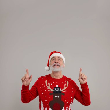 Noel süveteri giyen son sınıf öğrencisi ve gri arka planda bir şeye bakan Noel Baba şapkası.