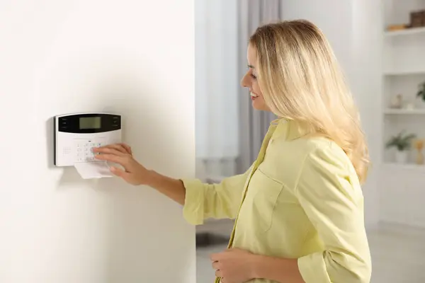 Woman entering code on home security system in room