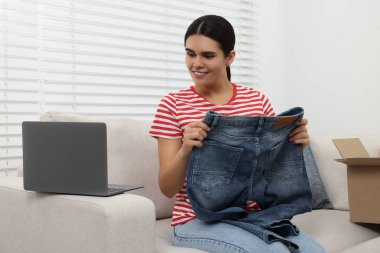 Evde dizüstü bilgisayar kullanarak yeni açılmış kotları olan genç bir kadın. İnternetten alışveriş