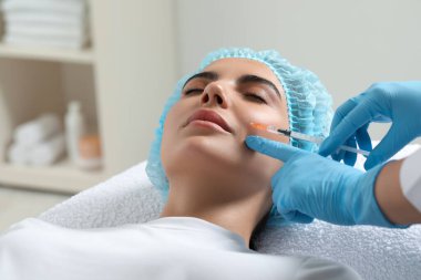 Doktor klinikteki genç bayana yüz enjeksiyonu yapıyor. Estetik ameliyat
