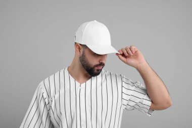 Açık gri arka planda şık beyaz beysbol şapkalı bir adam.