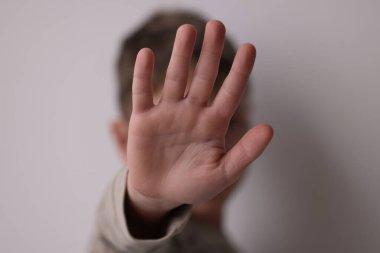 Çocuk istismarı. Açık gri arka planda jestleri durduran çocuk, seçici odaklanma