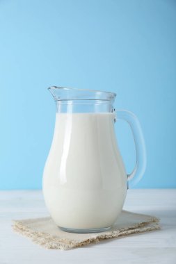 Açık mavi arka planda beyaz ahşap masada bir sürahi taze süt