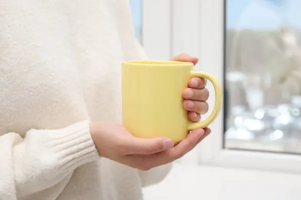 Woman holding yellow mug indoors, closeup. Mockup for design