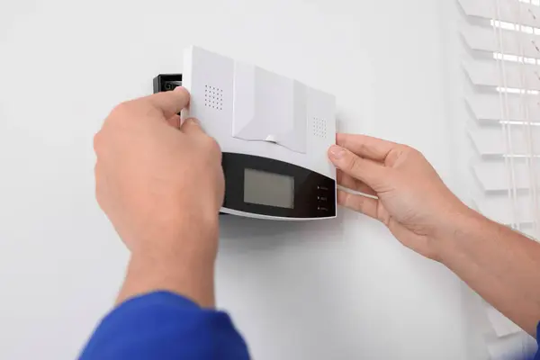 Man installing home security alarm system on white wall indoors, closeup