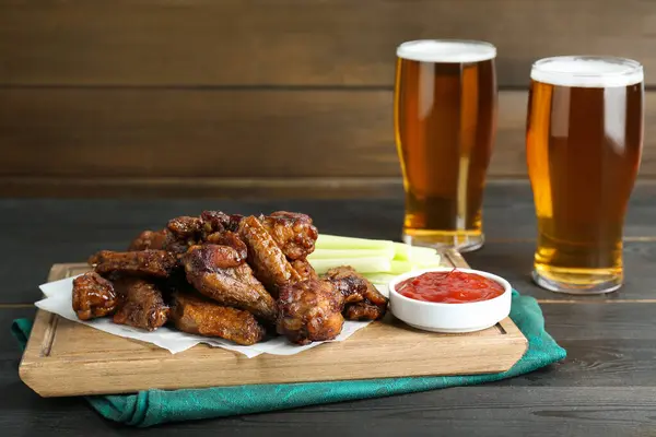 Delicious chicken wings served with beer on black wooden table