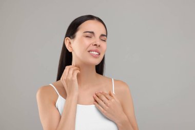 Alerji yüzünden acı çekiyor. Açık gri arka planda boynunu kaşıyan genç bir kadın.