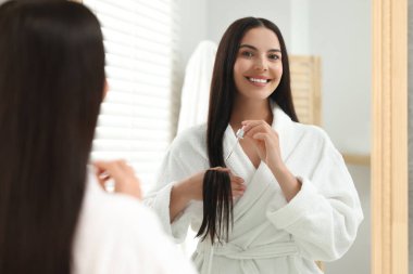 Güzel bir kadın evde saç serumu uyguluyor, aynada yansıması var. Kozmetik ürünü