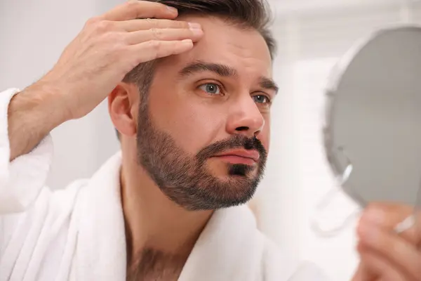 Man with skin problem looking at mirror indoors