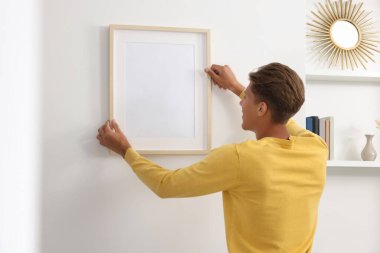 Genç adam beyaz duvarlara resim çerçevesi asıyor.