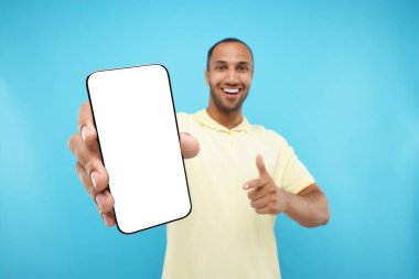 Genç adam elinde akıllı telefonu gösteriyor ve açık mavi arka planda ona işaret ediyor, seçici odaklanma. Tasarım için model