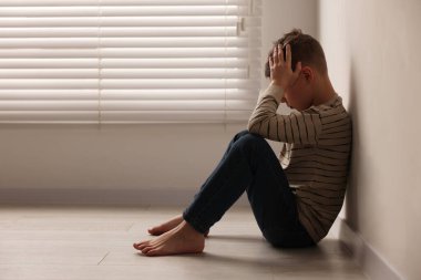 Çocuk istismarı. Kapalı alanda bej duvarın yanında oturan üzgün çocuk, mesaj için yer var.