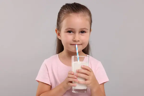 軽い灰色の背景にガラスから新鮮なミルクを飲むかわいい少女 — ストック写真