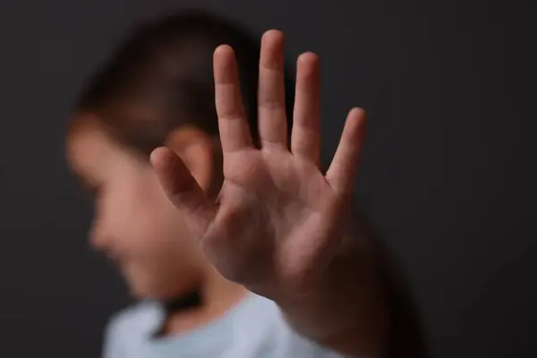 Child abuse. Little girl doing stop gesture on dark background, selective focus