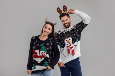 Mutlu genç çift, gri arka planda Noel süveteri ve ren geyiği başlığı takıyor.