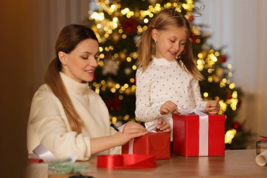 Noel hediyelerini paketliyorum. Anne ve küçük kızı evde hediye kutularını kurdeleyle süslüyorlar.