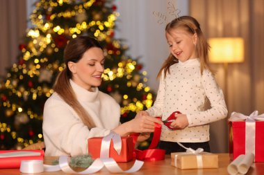 Noel hediyelerini paketliyorum. Anne ve küçük kızı evde kurdeleyle hediye kutusunu dekore ediyorlar.