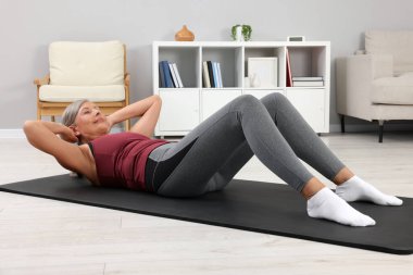 Spor giyim bölümündeki son sınıf kadın evde spor paspası üzerinde egzersiz yapıyor.