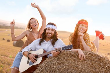 Güzel hippi kadınlar, arkadaşlarının tarlada gitar çalışını dinliyorlar.