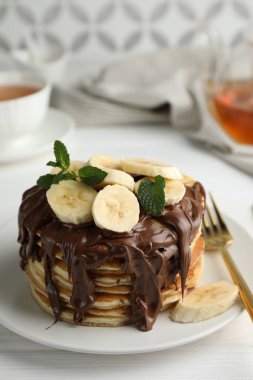Çikolata sürülmüş lezzetli gözlemeler, dilimlenmiş muz ve nane, beyaz masada servis ediliyor, yakın plan.