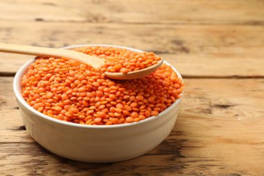 Tabakta çiğ kırmızı mercimek ve tahta masada kaşık, yakın plan. Metin için boşluk