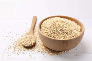 Kuru kinoa tohumları kasede ve kaşıkla beyaz fayanslı masada.