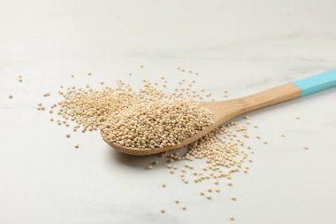 Beyaz mermer masanın üzerinde kuru kinoa tohumları olan kaşık, yakın plan.