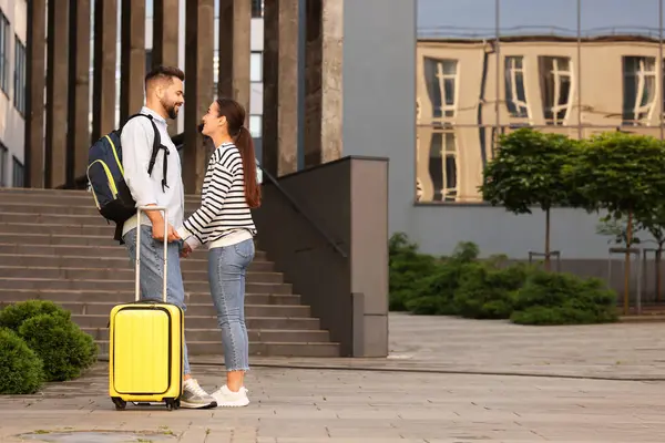 Long-distance relationship. Man with luggage holding hands with his girlfriend near building outdoors