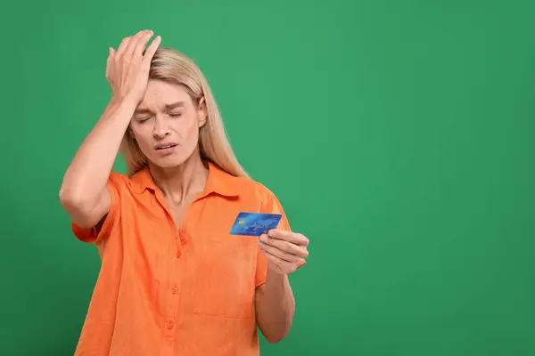 Stressed woman with credit card on green background, space for text. Be careful - fraud