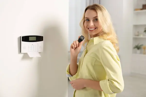 Home security system. Smiling woman with alarm key fob in room