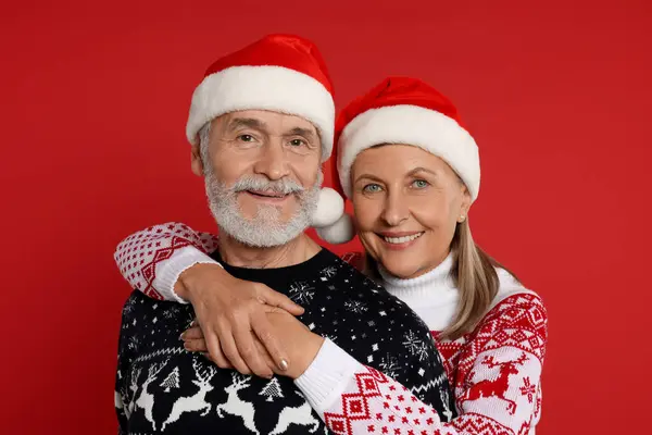 Couple Aîné Pulls Noël Chapeaux Père Noël Sur Fond Rouge — Photo