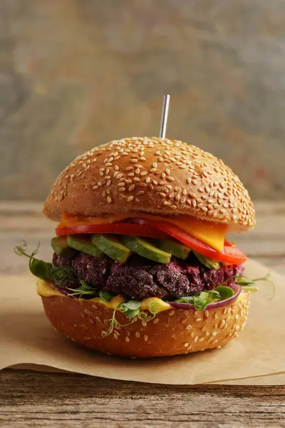 Tasty vegetarian burger with beet cutlet, cheese, avocado and tomato on wooden table