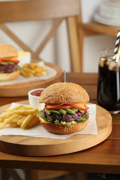 Tasty vegetarian burger served with french fries and soda drink on wooden table
