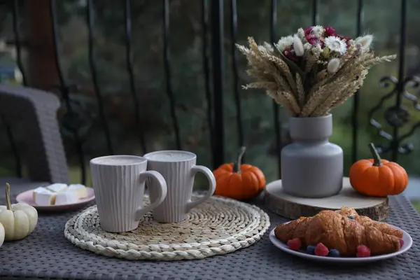 Snacking outdoors. Rattan table with cups of drink, croissants and autumn decor on terrace