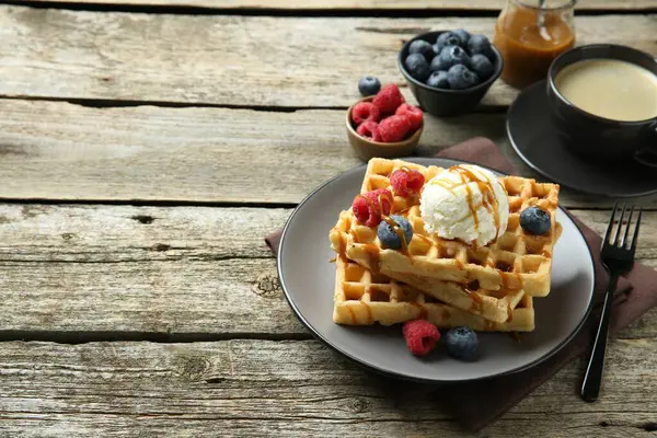 Dondurma, böğürtlen ve ahşap masada karamel soslu leziz Belçika waffleları.