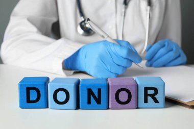 Sözcük donörü tahta küplerden yapılmış. Doktor beyaz masada deftere yazı yazıyor, yakın plan.