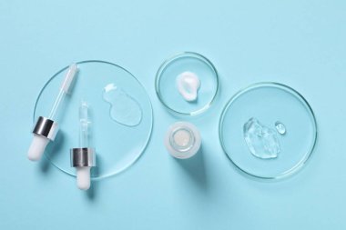 Açık mavi arka planda kozmetik serum, şişe ve pipetlerden örnekler içeren petri kapları düz.