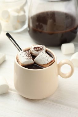 Bir fincan aromatik sıcak çikolata, marşmelov ve beyaz ahşap masa üzerine kakao tozu.