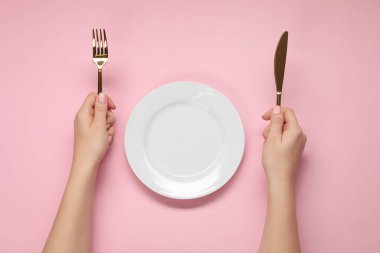 Pembe masadaki boş tabağın yanında çatal ve bıçak tutan kadın.