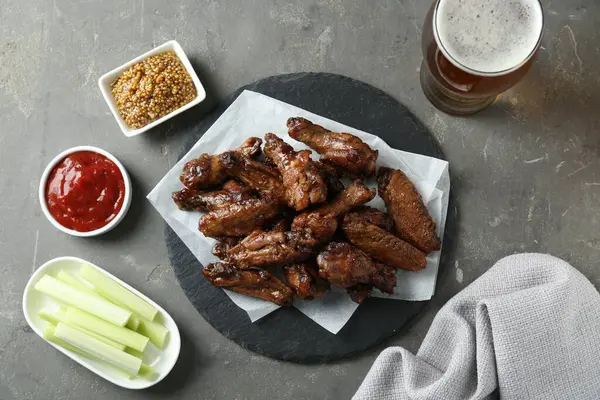 Delicious chicken wings served with beer on grey table, flat lay