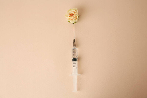 Medical syringe and beautiful rose on beige background, top view