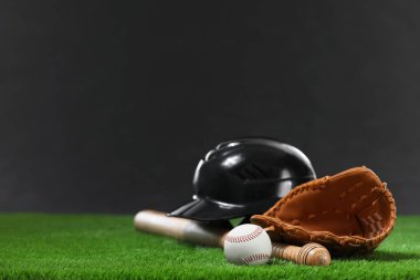 Beyzbol sopası, beysbol kaskı, deri eldiven ve yeşil çimlerin üzerinde koyu arka planda duran top. Metin için boşluk