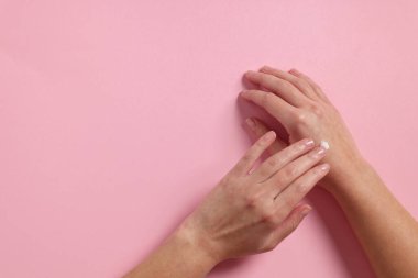 Kadın pembe arka planda kozmetik krem sürüyor. Metin için boşluk