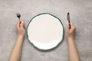 Çatal ve bıçak taşıyan kadın gri desenli masada, boş tabağın yanında.