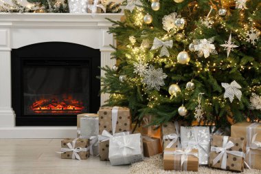 Evdeki şöminenin yanındaki güzel Noel ağacının altında bir sürü hediye kutusu var.