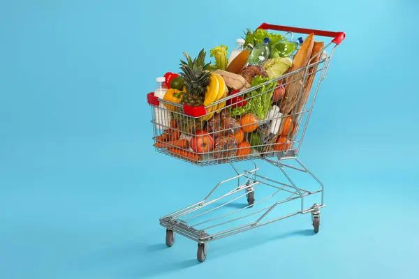 Shopping cart full of groceries on light blue background