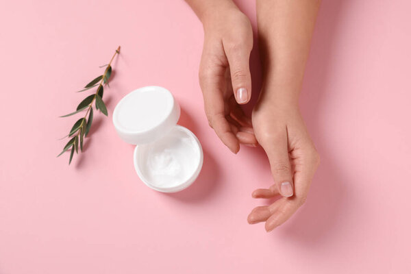 Woman with jar of hand cream and leaves on pink background, top view