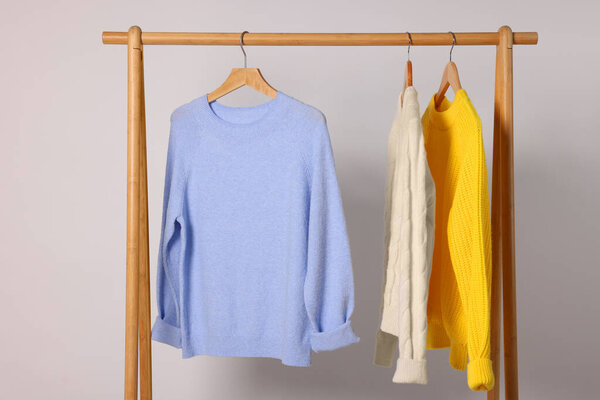 Rack with different warm sweaters on light background