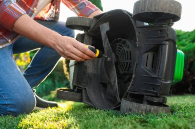 Tornavidalı bir adam dışarıda çim biçme makinesini tamir ediyor.