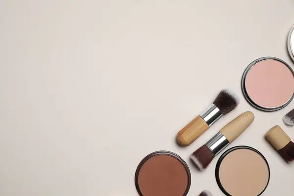 Different face powders and makeup brushes on beige background, flat lay. Space for text